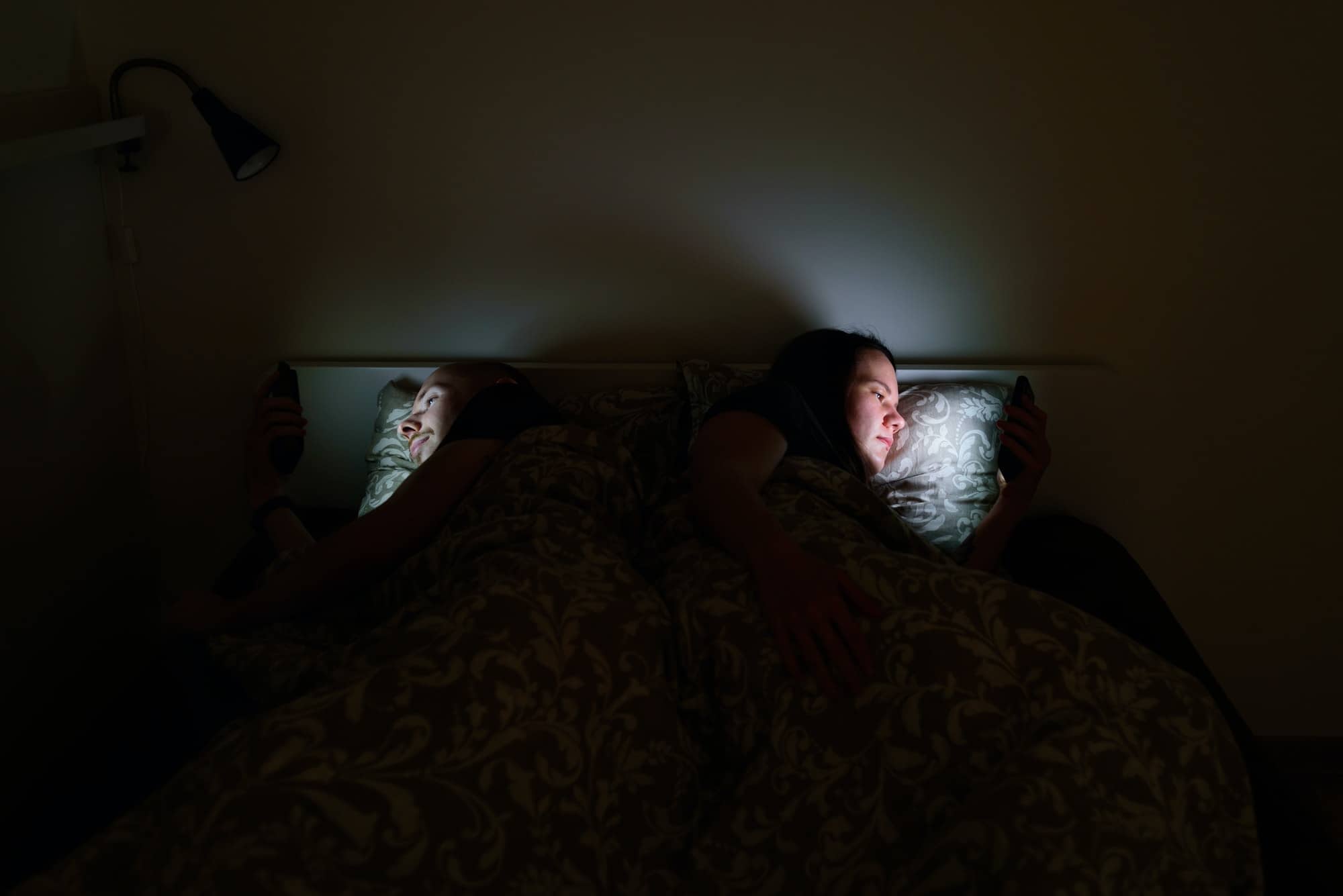 Couple using phones lying in bed before sleep