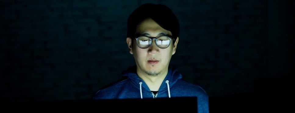 Young Asian man using computer in the dark room - unhealthy eyes concept.